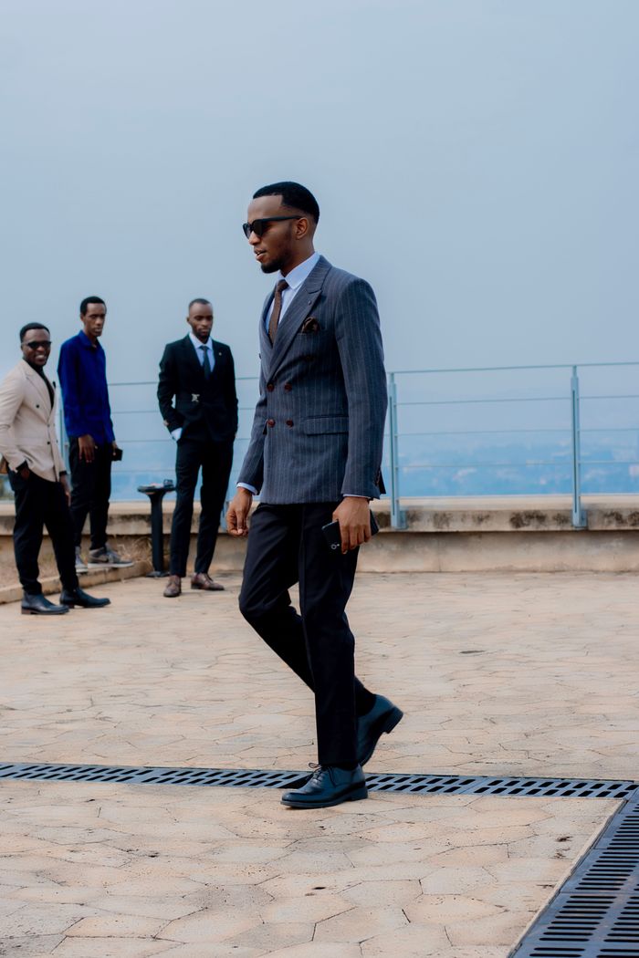 A group of stylish men in formal suits have a rooftop meeting with a city view.