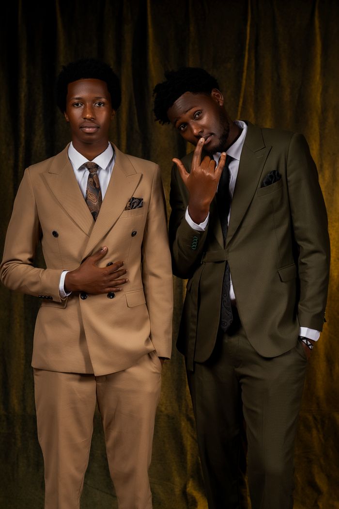 Stylish portrait of two men in formal suits against a warm backdrop, showcasing modern Kigali fashion.